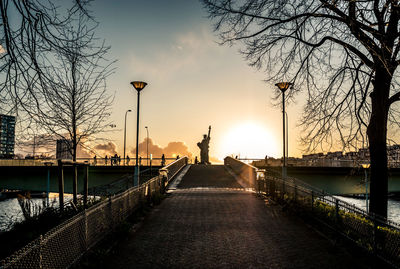 Path leading to statue by river against sky during sunset