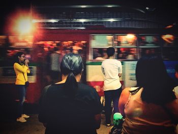 Rear view of people walking on illuminated street at night