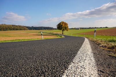 Surface level of road amidst field against sky