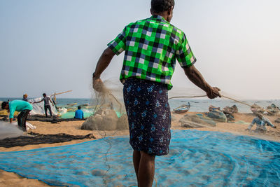 Rear view of people standing on beach against clear sky