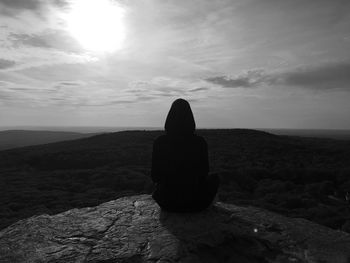 Rear view of woman sitting on rock against sky