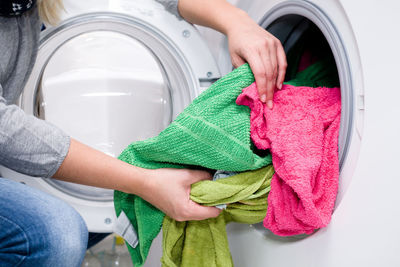 Midsection of woman putting clothes in washing machine