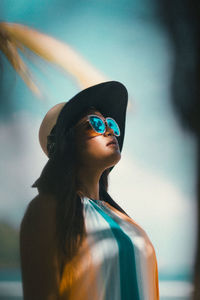 Woman wearing sunglasses and hat looking away against sky