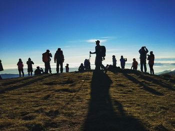 Silhouette people on mountain against blue sky