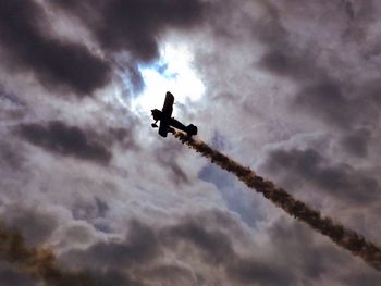 Low angle view of silhouette airplane against cloudy sky