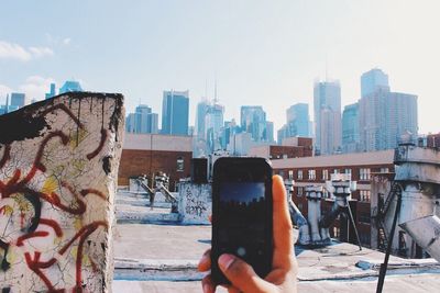 Cropped image of hand photographing cityscape from building terrace