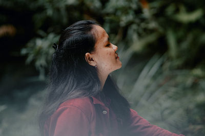 Mature woman looking away while standing against trees