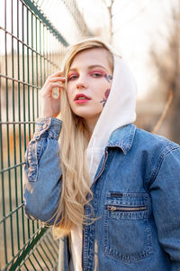 Portrait of beautiful young woman standing by fence