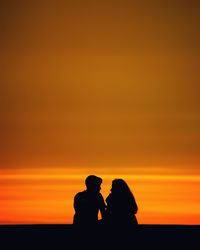 Silhouette people against orange sky during sunset