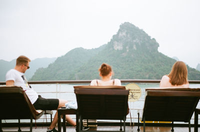 Rear view of people sitting on table against mountains