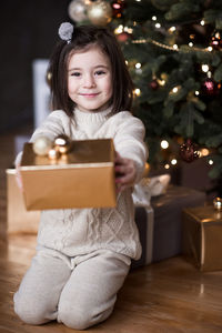 Portrait of cute girl giving gift box against christmas tree
