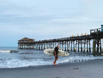 Woman on pier at beach against sky