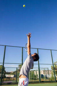 Man playing tennis on court against blue sky