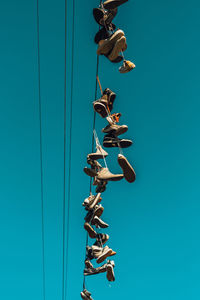 Low angle view of shoes handing on cable against clear blue sky