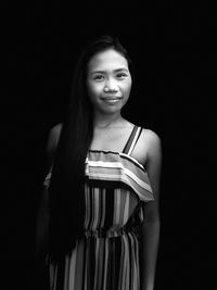 Portrait of smiling woman standing against black background