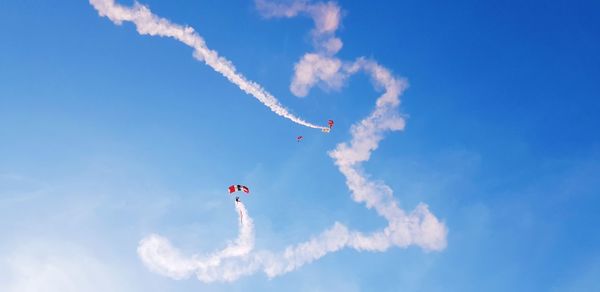 Low angle view of people paragliding against blue sky