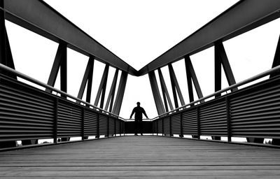 Rear view of woman walking on footbridge against clear sky