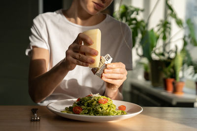 Woman hands grating parmesan cheese in pasta with sauce pesto, fresh cherry tomatoes