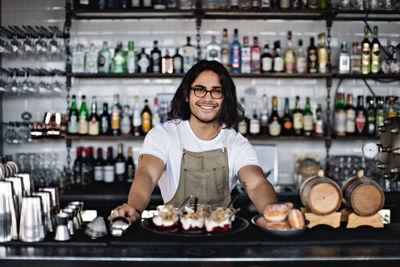 Portrait of smiling owner with food standing at counter in restaurant