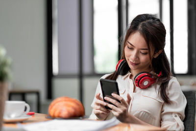 Young woman using mobile phone while sitting on table