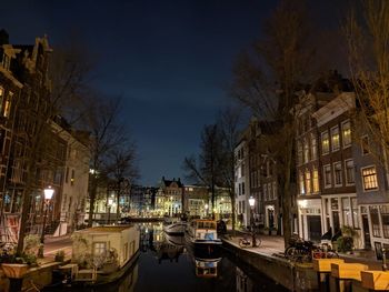 Boats moored in canal amidst buildings in city at night