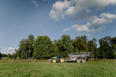 Tractor on field against tree under cloudy sky