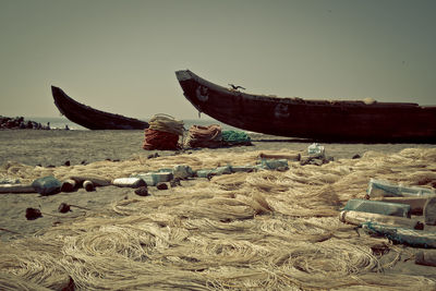 Boats moored at beach by fishing nets against clear sky