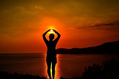 Silhouette woman standing by sea against orange sky