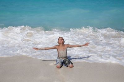 Shirtless boy with arms out
stretched relaxing on shore at beach