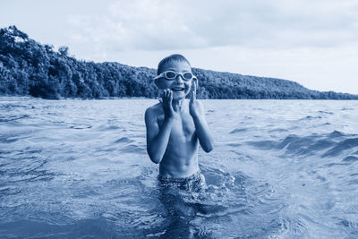 Portrait of shirtless boy in lake against sky