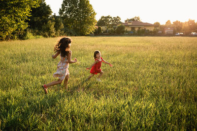 Two girls in dresses running one after another in the evening field
