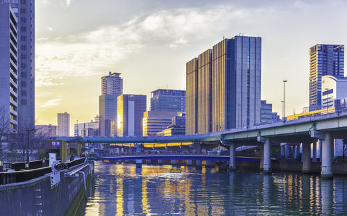 Bridge over river by buildings against sky in city