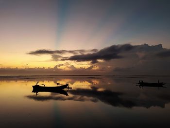 Silhouette boat in sanur beach against sky during sunrise