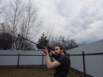 Side view of young man shooting gun at backyard