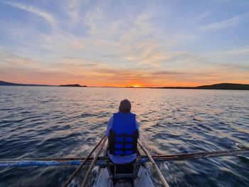 Rear view of man in sea against sky during sunset