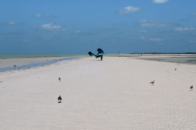 Rearview of a man walking on the beach against sky with kitesurfing