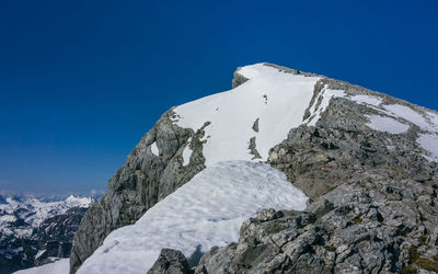 Low angle view of snowcapped mountains against clear blue sky