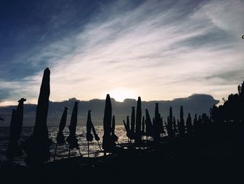 Silhouette wooden posts on beach against sky during sunset