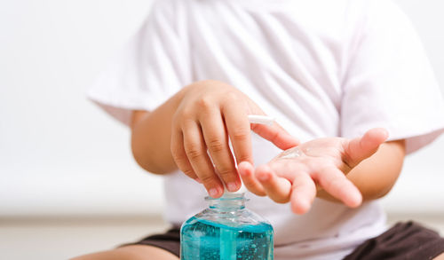 Midsection of boy using hand sanitizer at home