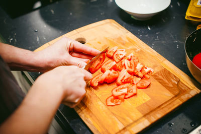 Cropped hand of woman chopping tomatoes on cutting board in kitchen