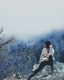 Man sitting on rock against sky during winter