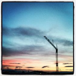 Low angle view of crane against cloudy sky