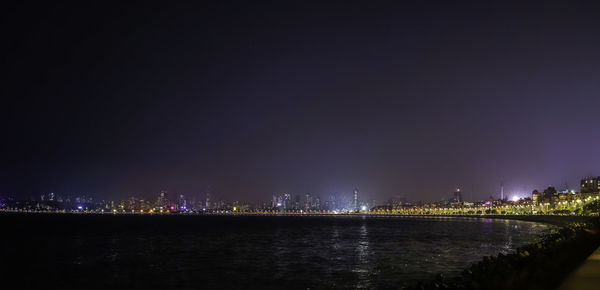 Illuminated city by river against sky at night