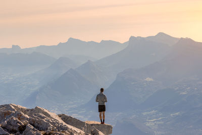 Rear view of man standing on cliff against sky