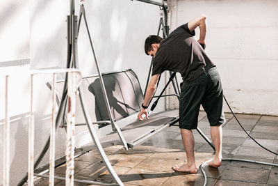 A young guy washes a garden swing with a kercher.