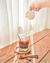 Midsection of person pouring drink in glass on table