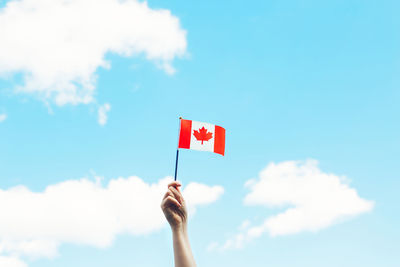 Human hand arm waving canadian flag against blue sky.  national canada day on 1st of july outdoor.