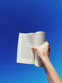 Cropped hand of person holding paper against blue background