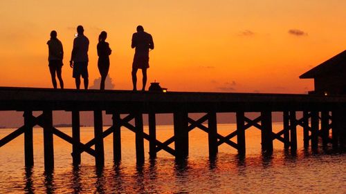 Silhouette people on bridge over sea against sky during sunset