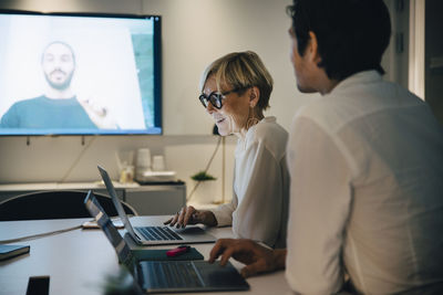 Smiling businesswoman sitting with businessman in board room during video conference